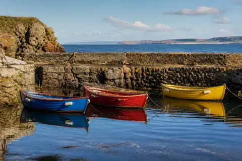 Blue, red and yellow rowing boats moored by a stone harbour wall