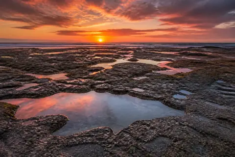 Flat rocks with pools reflecting an orange and pink sunset sky